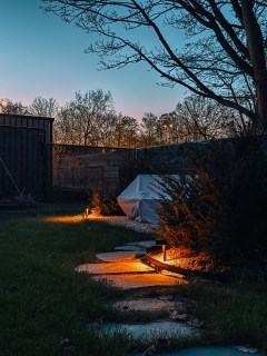 Modern backyard garden pathway with warm outdoor lighting at dusk and stone stepping path